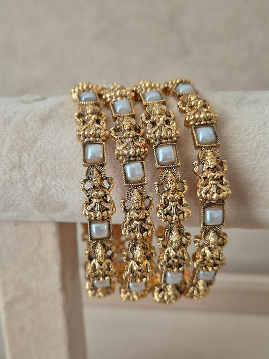 A stack of four traditional Indian antique gold-plated bangles set with intricate deity motif carvings and decorated  square white stone accents, by naitri.in