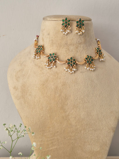 Modern Indian ethnic imitation jewelry set including a golden brass alloy floral-themed choker necklace embedded with green gemstones and white pearl drops, by naitri.in