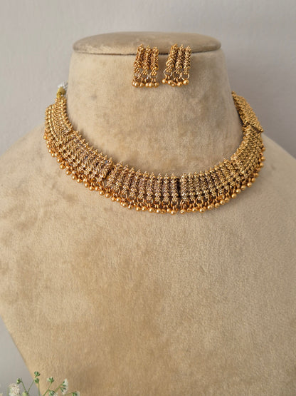 Modern Indian traditional imitation jewelry set including a golden brass alloy collar choker necklace with detailed filigree-style metalwork and delicate hanging beads, by naitri.in