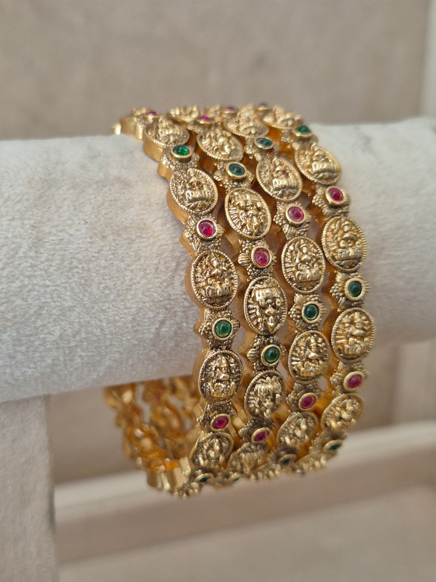 close-up of Naitri Hemali premium gold ethnic bangle set with traditional Goddess motifs, filigree metalwork, and vibrant red and green stone embellishments by naitri.in