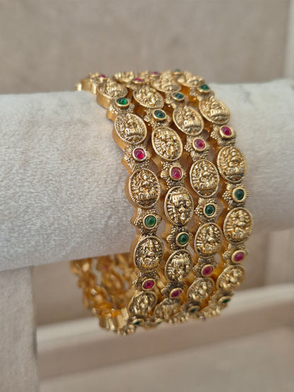 close-up of Naitri Hemali premium gold ethnic bangle set with traditional Goddess motifs, filigree metalwork, and vibrant red and green stone embellishments by naitri.in