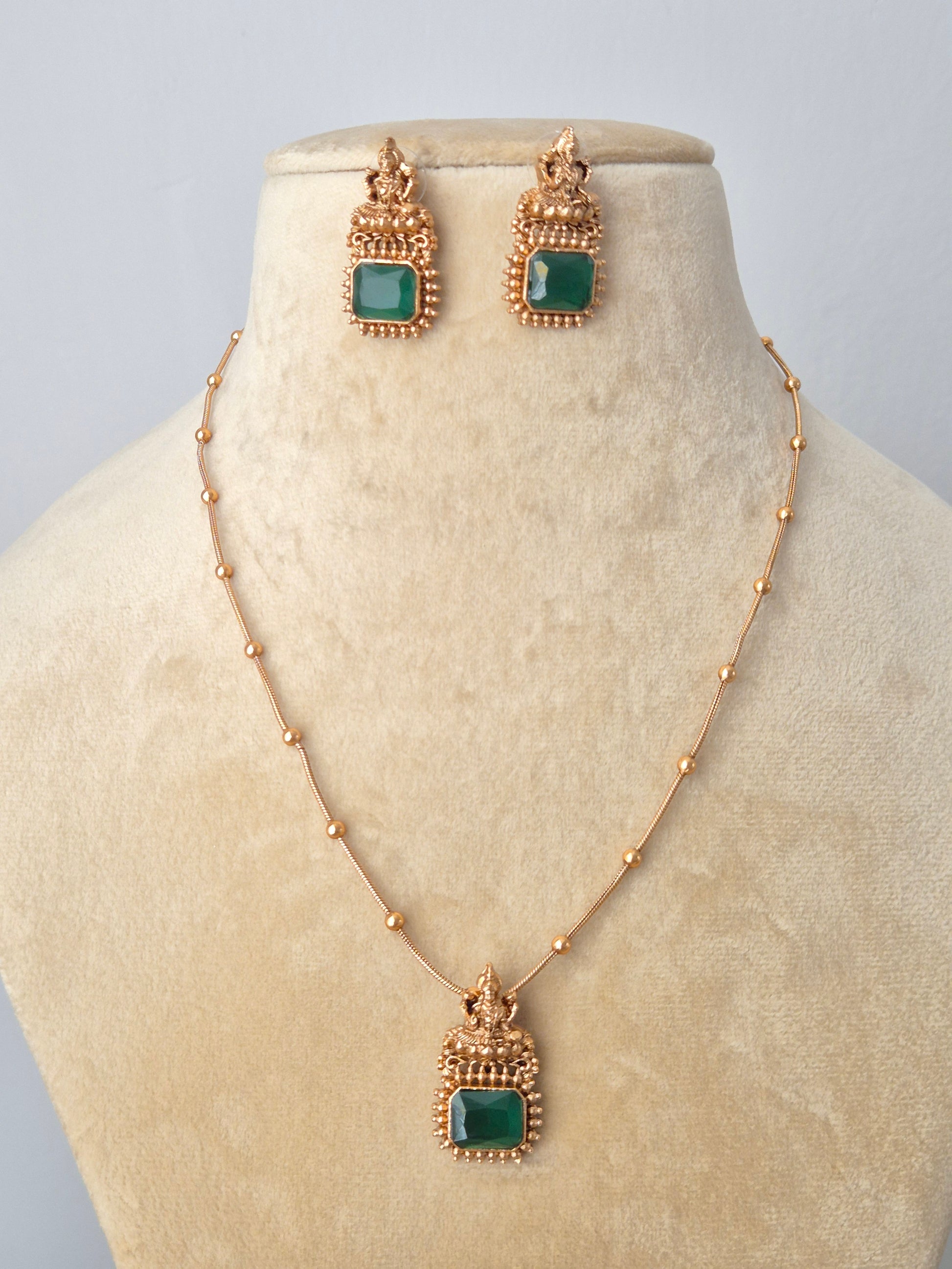 Close-up of a delicate golden brass chain with a rectangular green stone pendant surrounded by brass round ball type pearls, paired with matching green square earrings by naitri.in