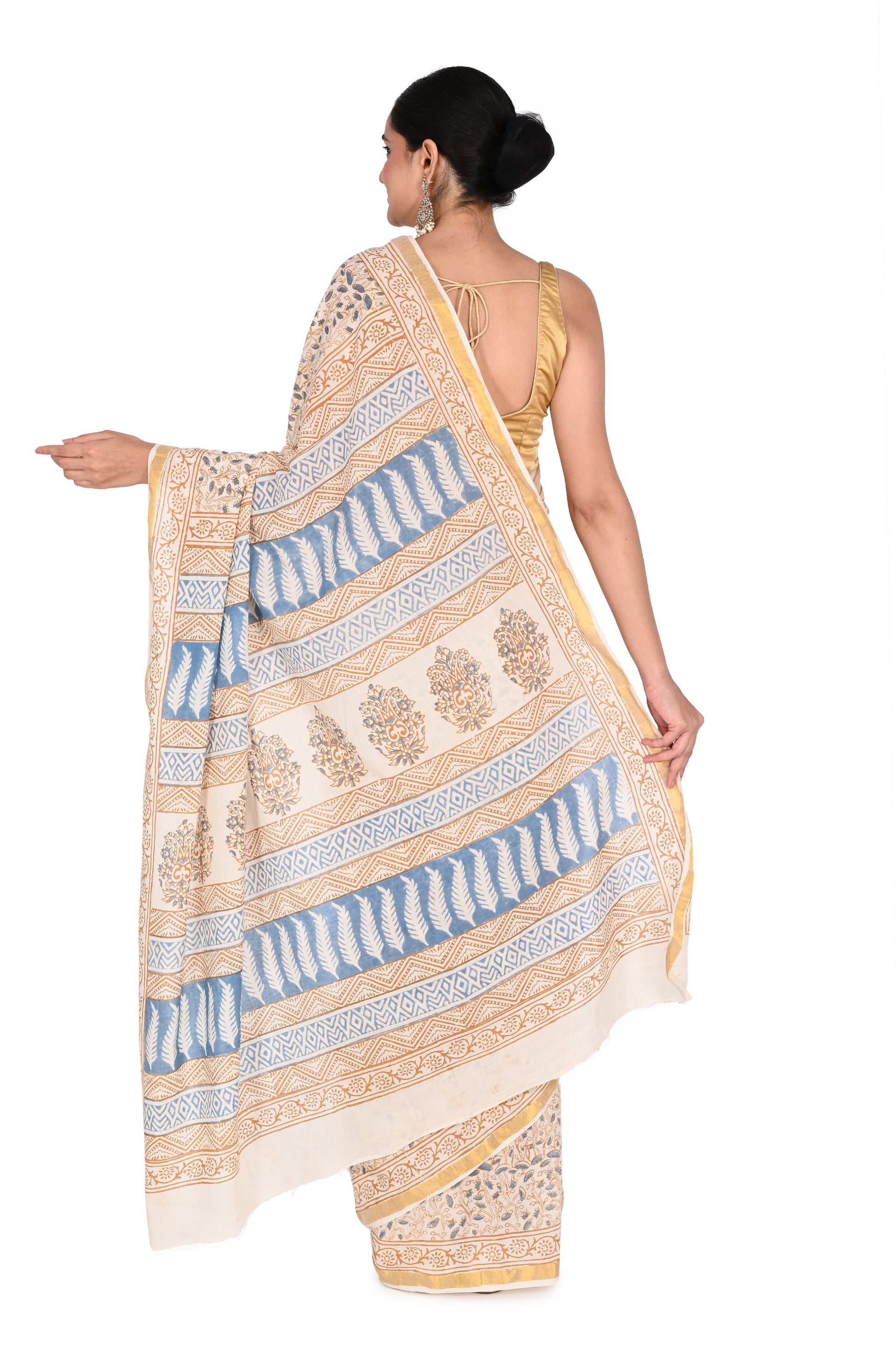 Full-length view of a woman wearing a white and beige cotton saree with small repeating blue patterns and a decorated vertical border by naitri.in