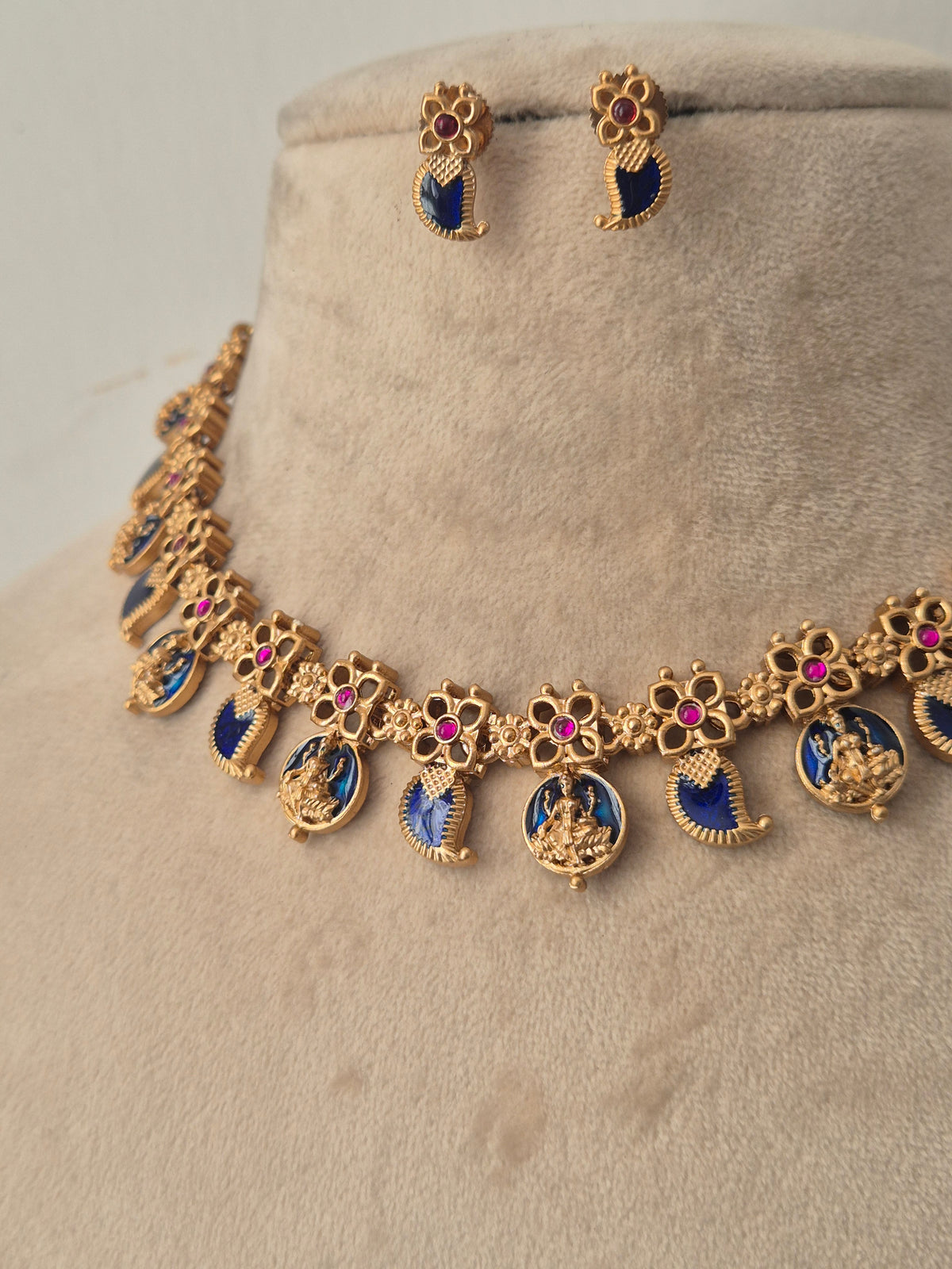 Gold-plated jewelry set featuring a necklace and matching earrings with blue enamel inlays, pink stone accents, and deity motifs, by naitri.in