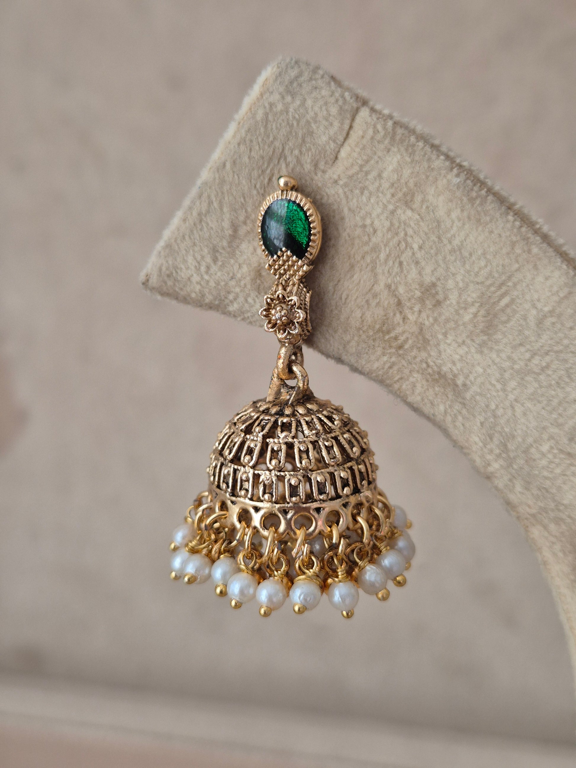 An ornate gold-toned jhumka earring with a green oval stone at the top and dangling pearl-like beads, by naitri.in