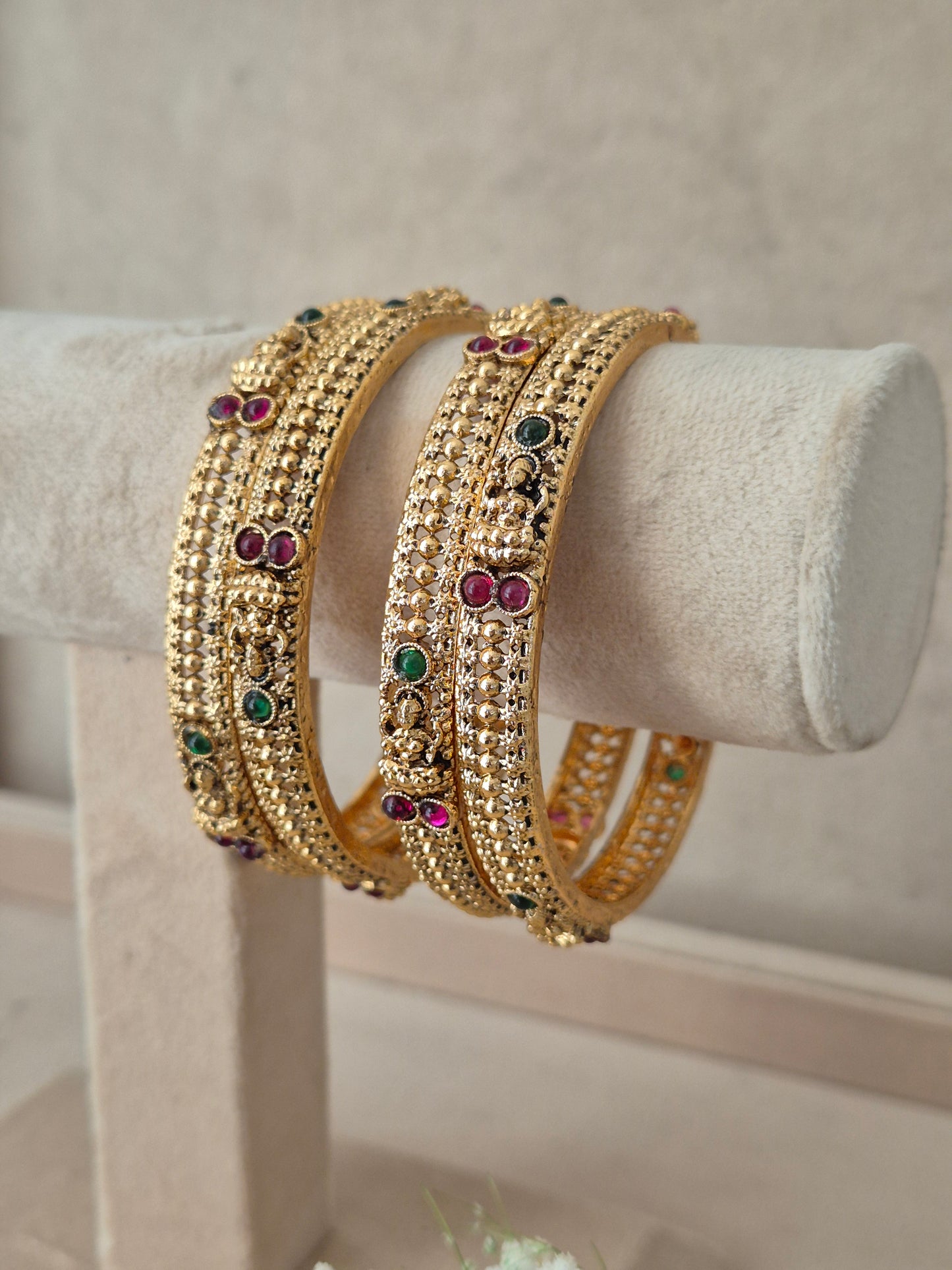Four gold-plated bangles decorated with small clear stones and colorful red and green gemstone accents, by naitri.in