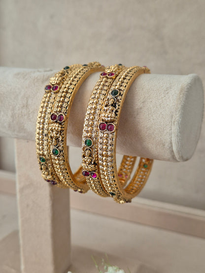 Four gold-plated bangles decorated with small clear stones and colorful red and green gemstone accents, by naitri.in