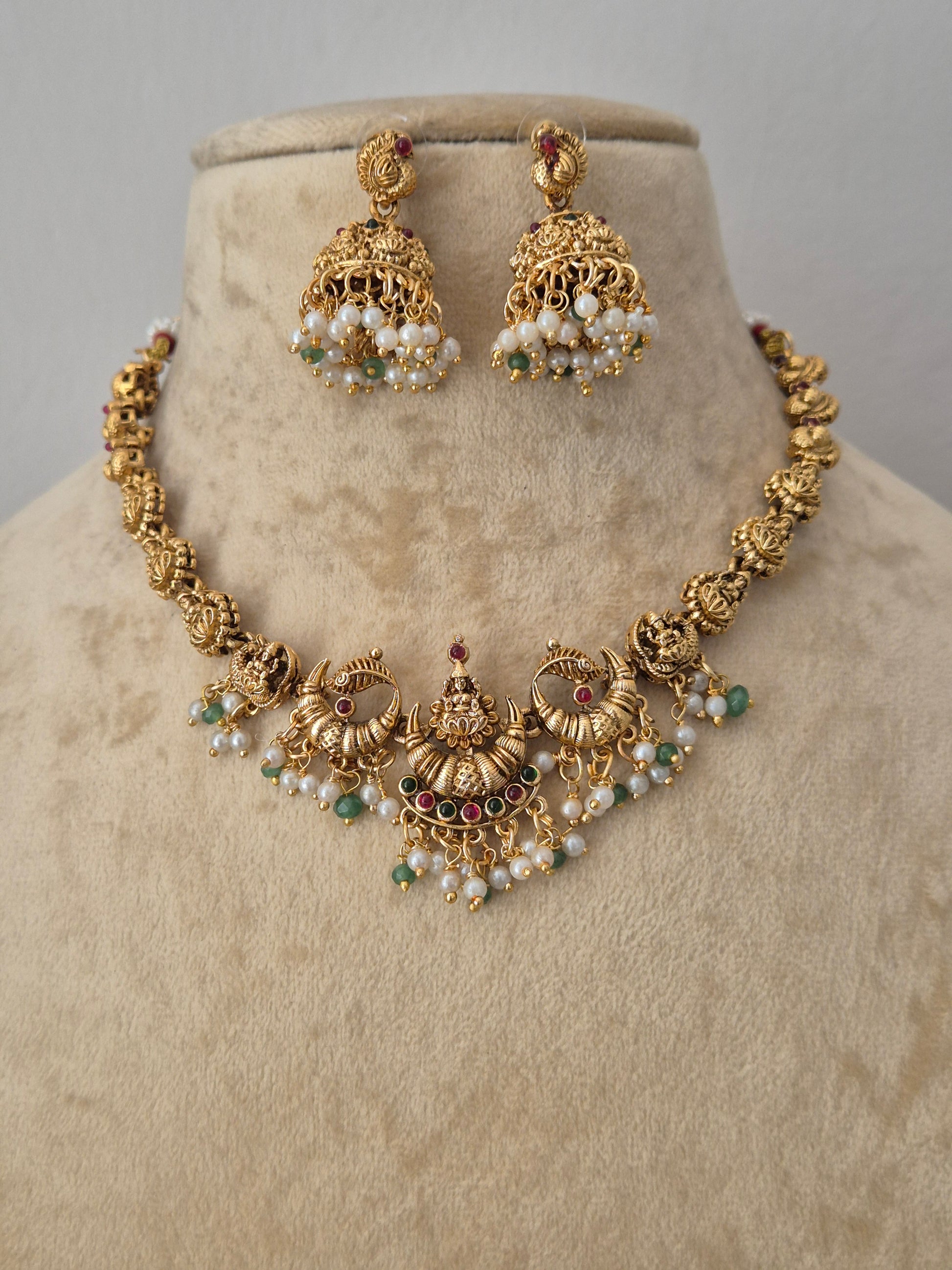 Gold-toned traditional Indian jewelry set featuring a jhumka earrings pair the pieces are decorated with white pearl-like beads, small green stones, and tiny red stones by naitri.in