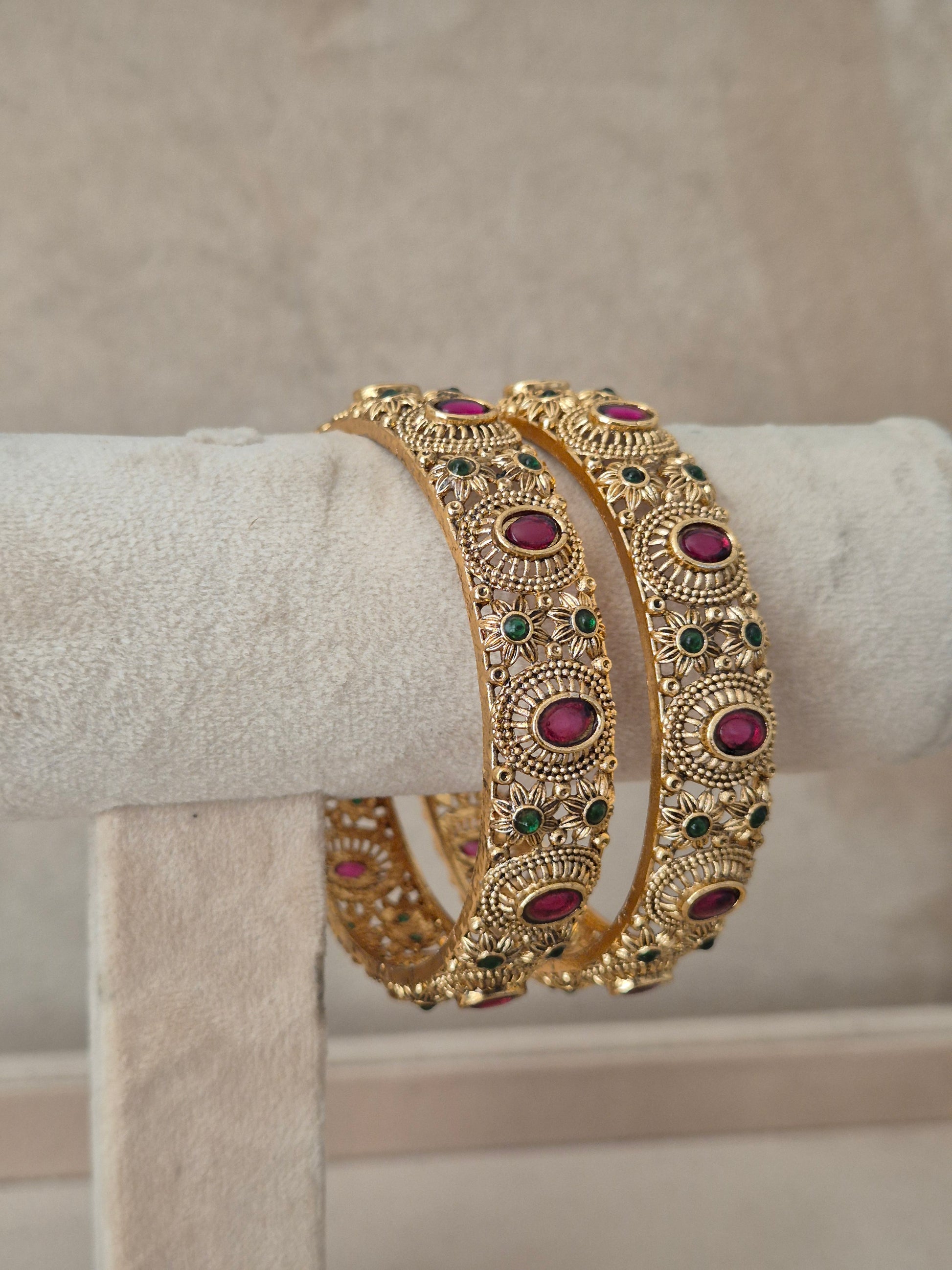  set of 2 antique gold-plated bangles featuring intricate floral filigree patterns studded with red and green stones, by naitri.in