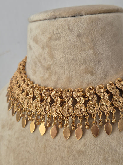 An ornate gold-toned statement necklace features a wide collar of textured floral and medallion motifs with dangling leaf-shaped charms by naitri.in