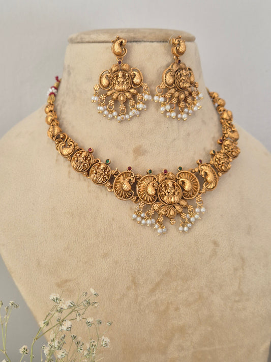 An ornate gold-toned traditional necklace and matching earrings Traditional gold-toned temple jewelry choker set with intricate circular motifs, goddess engravings, and white faux pearl drops, shown with matching dangle earrings by naitri.in