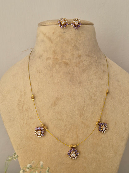 Minimalist gold-toned fine chain necklace featuring three dangling flower charms made of light purple gemstones and clear crystal centers, shown with coordinating lavender floral earrings by naitri.in