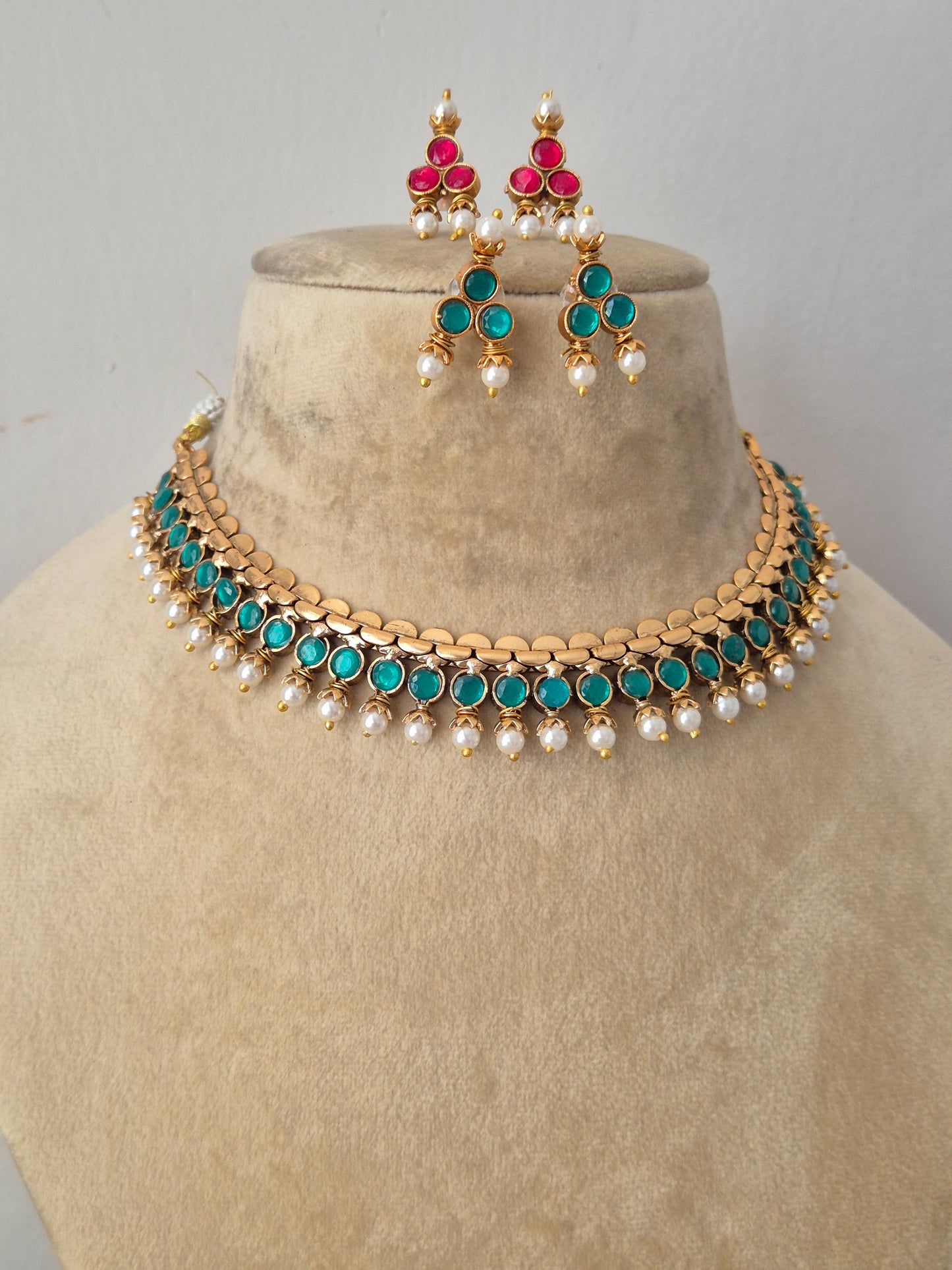Antique gold-plated ethnic choker set with a structured band of vibrant blue stones, delicate dangling white pearls, and coordinating floral stud earrings showcasing pink and green accents by naitri.in