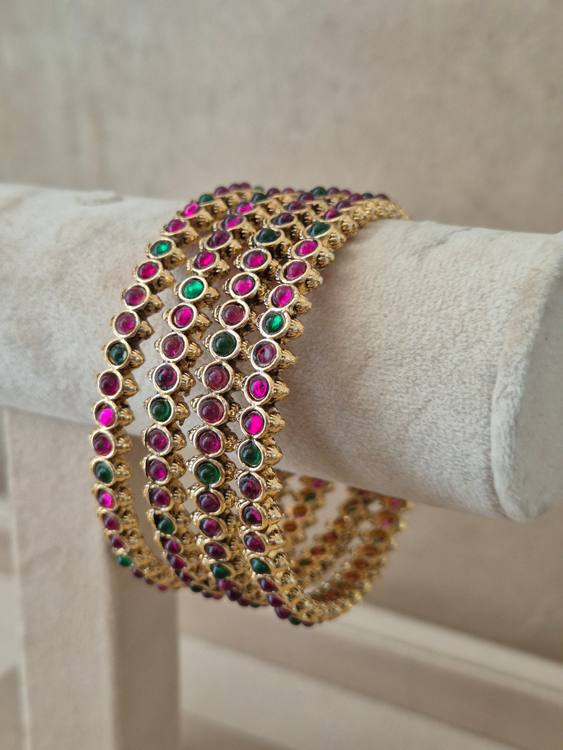 Close-up of Naitri Kadambari premium gold ethnic bangle set featuring traditional Indian festive jewelry style with alternating ruby red and emerald green stone embellishments. by naitri.in