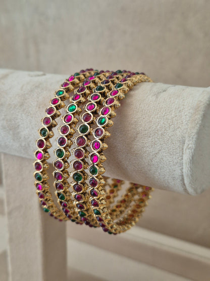 Close-up of Naitri Kadambari premium gold ethnic bangle set featuring traditional Indian festive jewelry style with alternating ruby red and emerald green stone embellishments. by naitri.in
