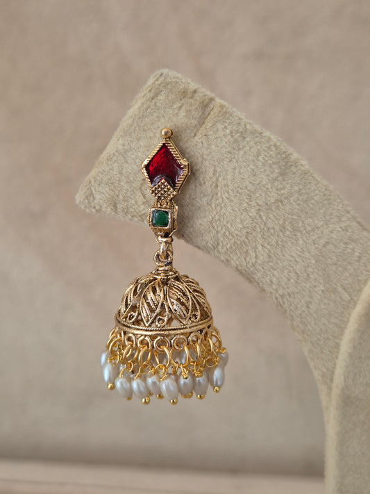 Close-up of Naitri Kalindi premium gold ethnic earrings showcasing traditional Indian temple jewelry craftsmanship with vibrant ruby red and emerald green gemstone accents and delicate pearl dangling beads by naitri.in