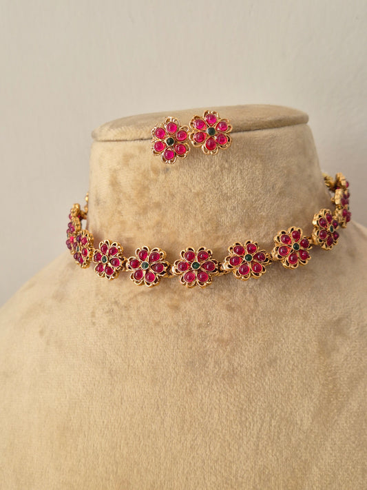 Gold-plated ethnic choker set showcasing a continuous chain of ruby-pink gemstone flowers with green stone centers, by naitri.in