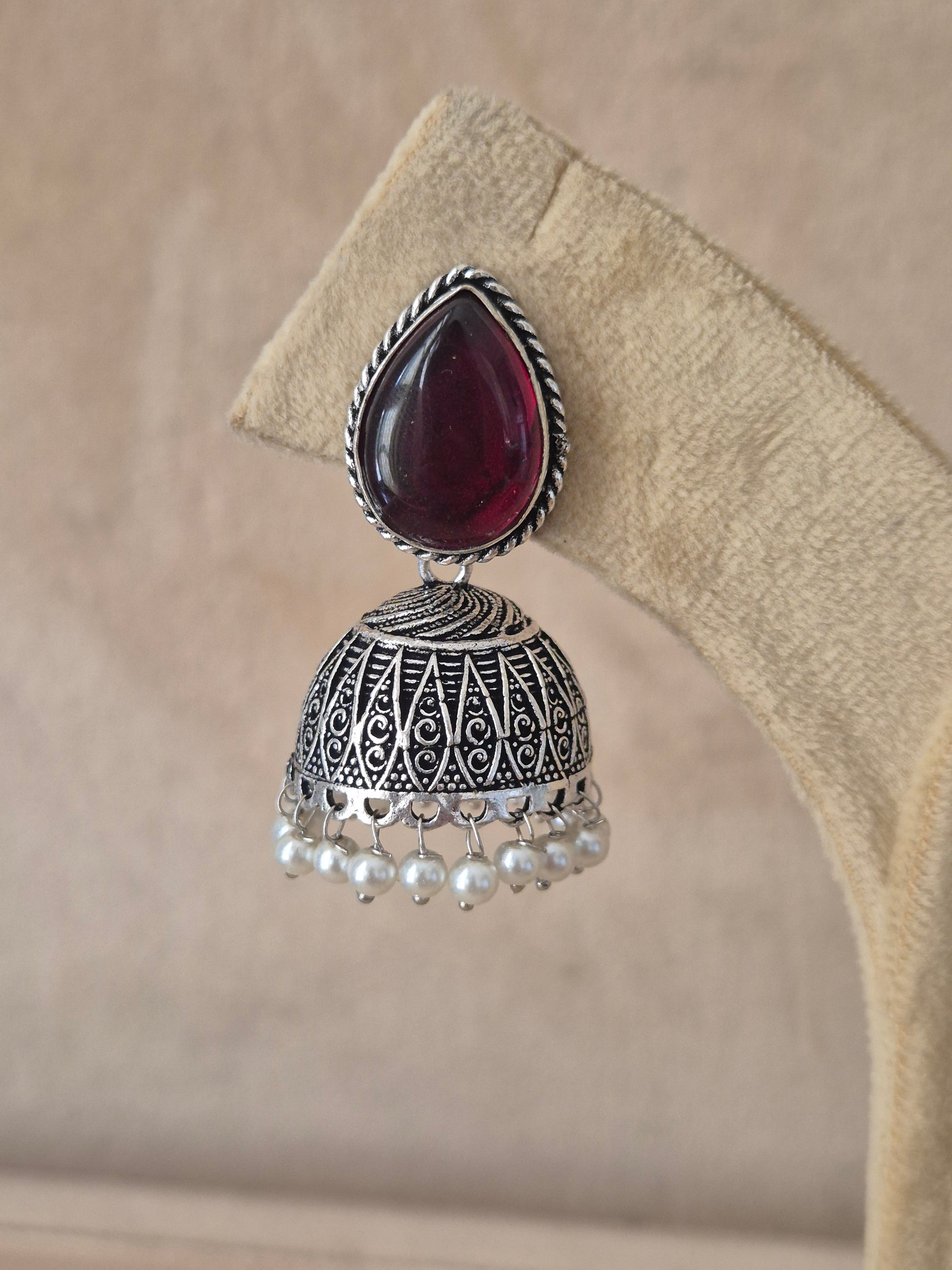 Modern Indian aesthetic silver-plated statement jhumkas featuring a vibrant purple focal stone and intricate metalwork by naitri.in