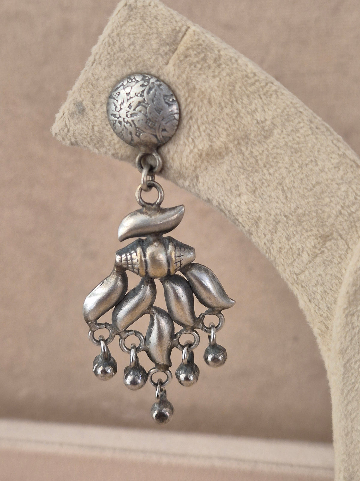 A silver-toned dangling earring with a round textured top and a shell-shaped charm holding several small dangling beads, by naitri.in