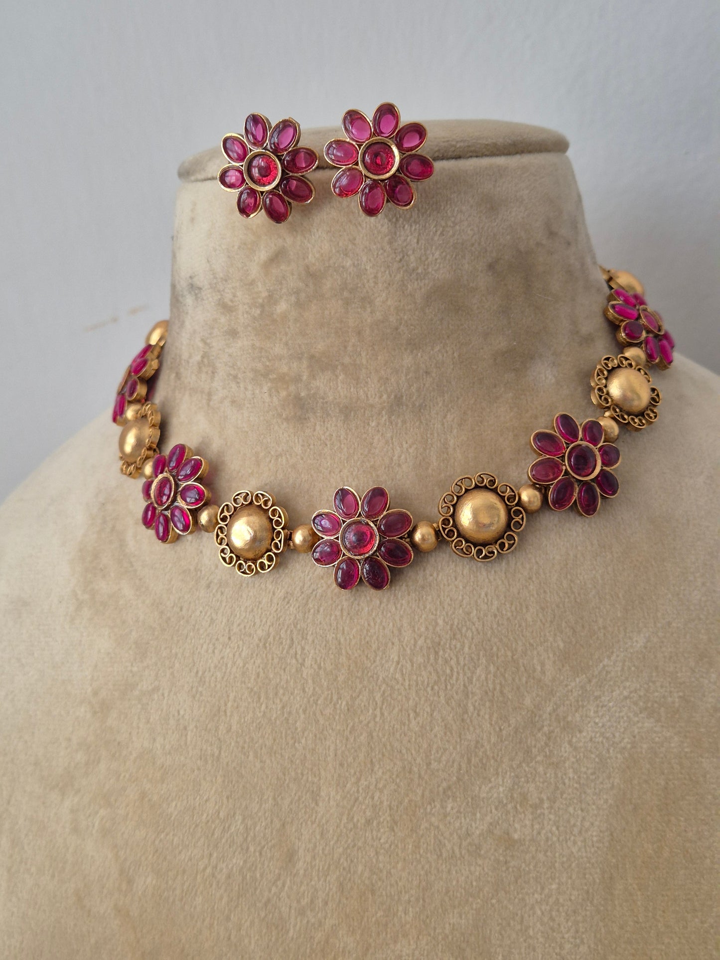 Modern Indian ethnic imitation jewelry set including a golden brass alloy choker necklace embedded with vibrant ruby-red stones in a floral pattern, by naitri.in