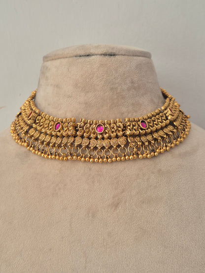 Traditional gold choker necklace featuring intricate antique detailing with pink stone accents and small dangling beads, with matching bell-shaped jhumka earrings by naitri.in