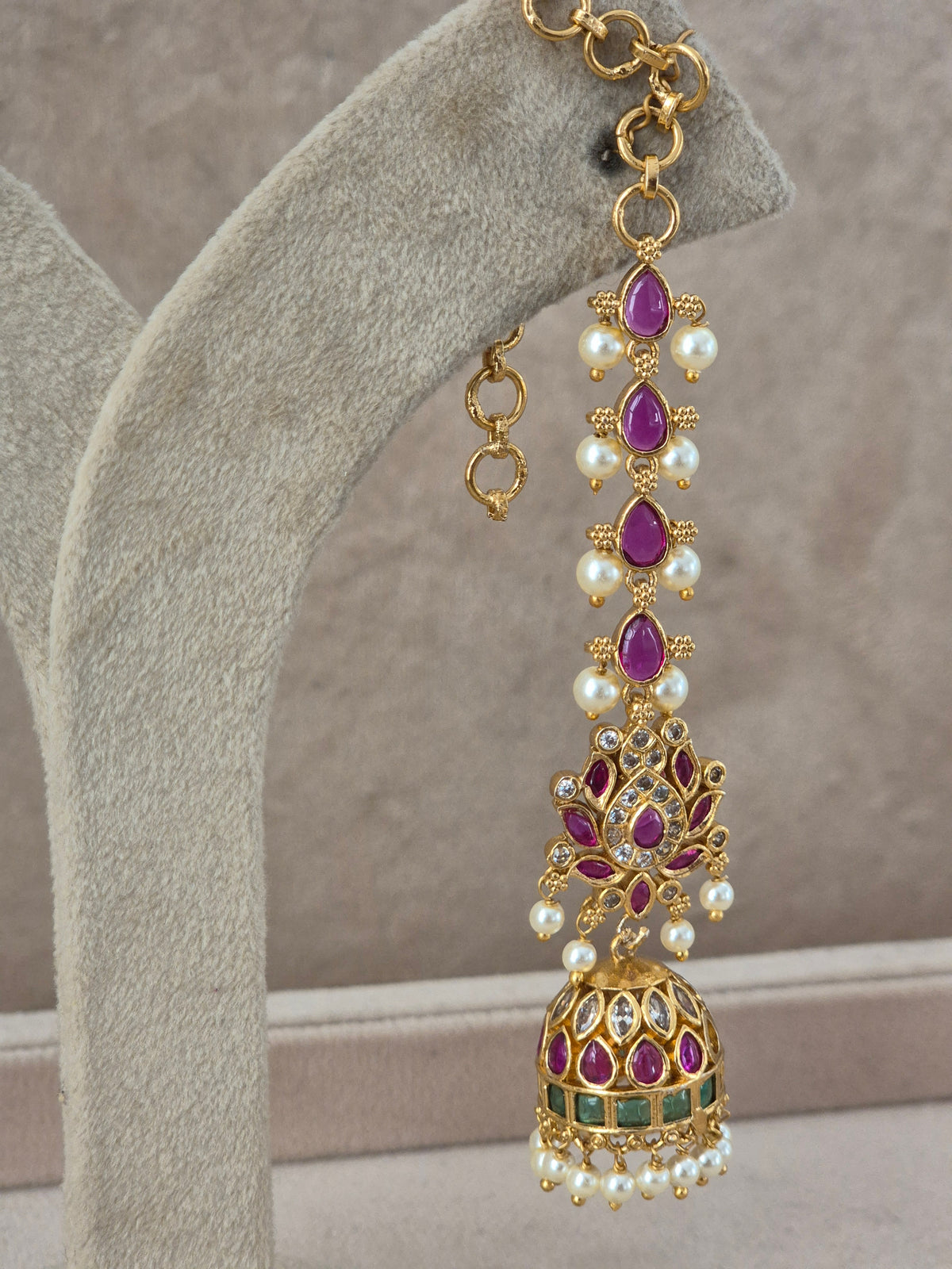 An ornate gold-toned jhumka earring with teardrop-shaped purple gemstones, white faux pearls, and small green stone accents, by naitri.in