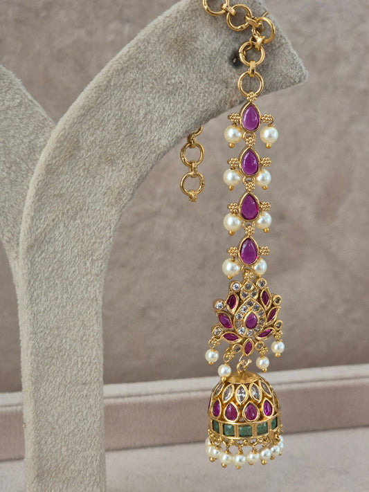 An ornate gold-toned jhumka earring with teardrop-shaped purple gemstones, white faux pearls, and small green stone accents, by naitri.in