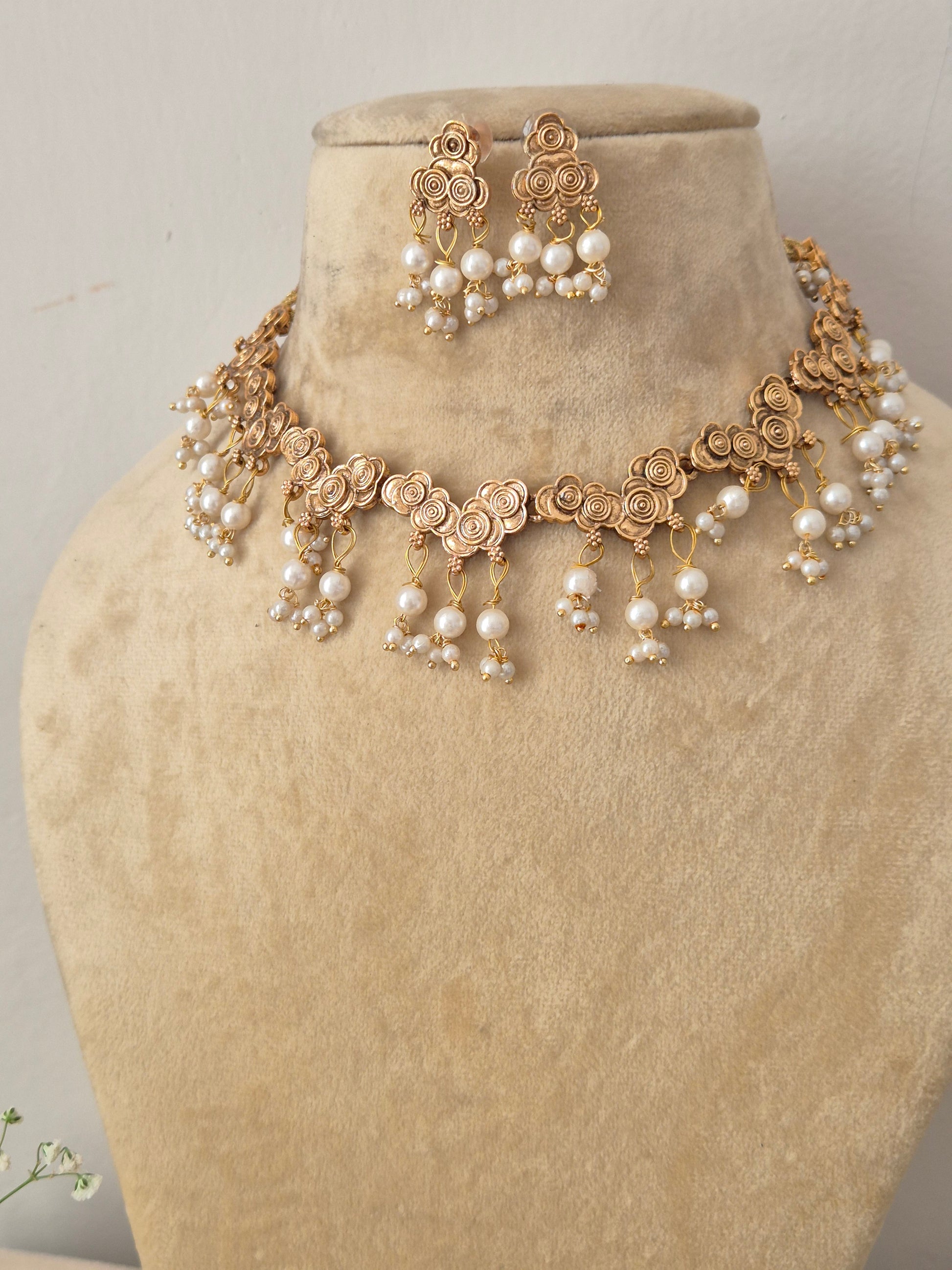 Modern Indian traditional imitation jewelry set including a golden brass alloy choker necklace with delicate floral detailing and cascading white pearl tassels by naitri.in
