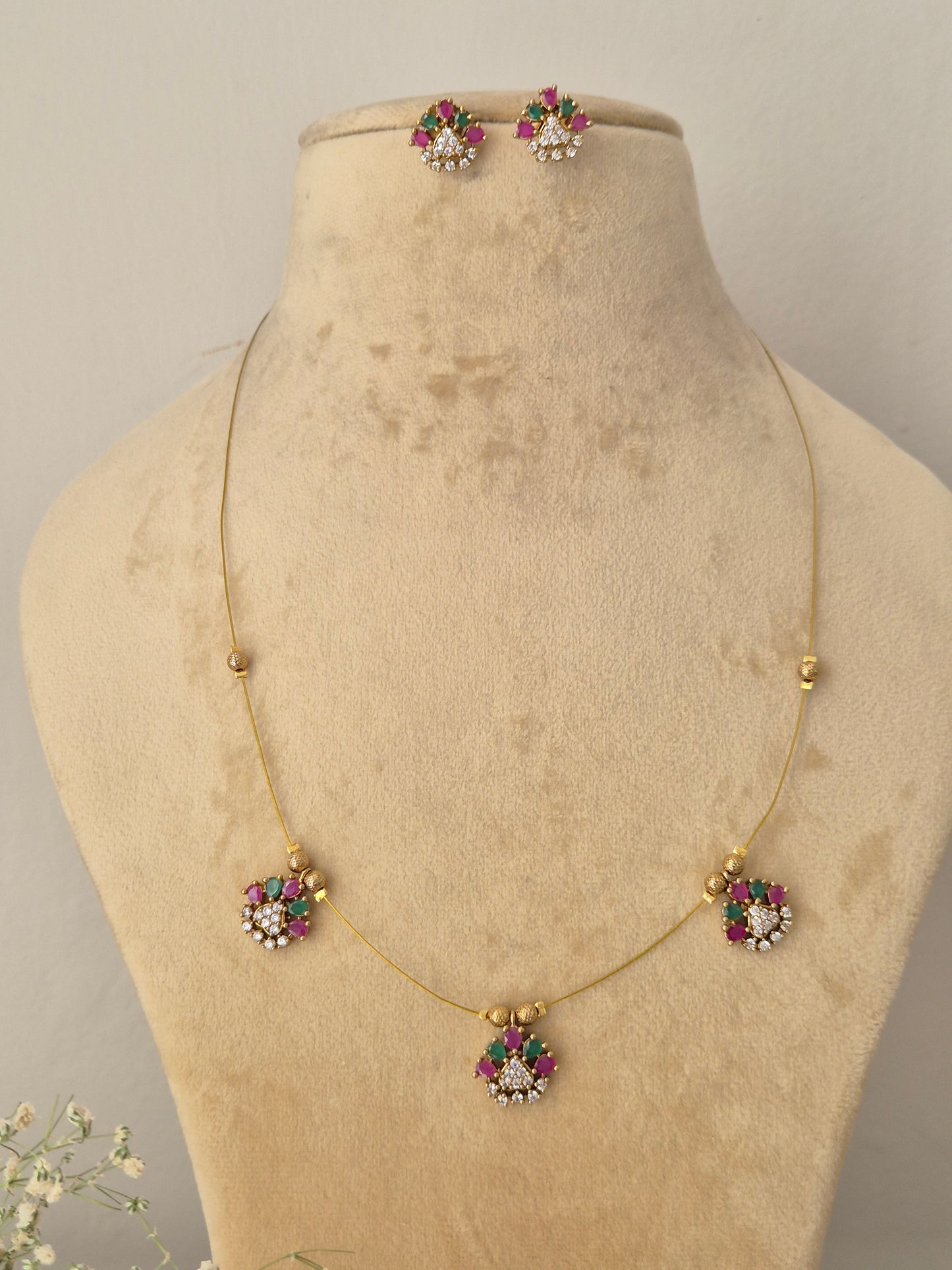 Minimalist gold-toned fine chain necklace featuring three dangling flower charms with pink and green stone petals, coordinating floral stud earrings by naitri.in