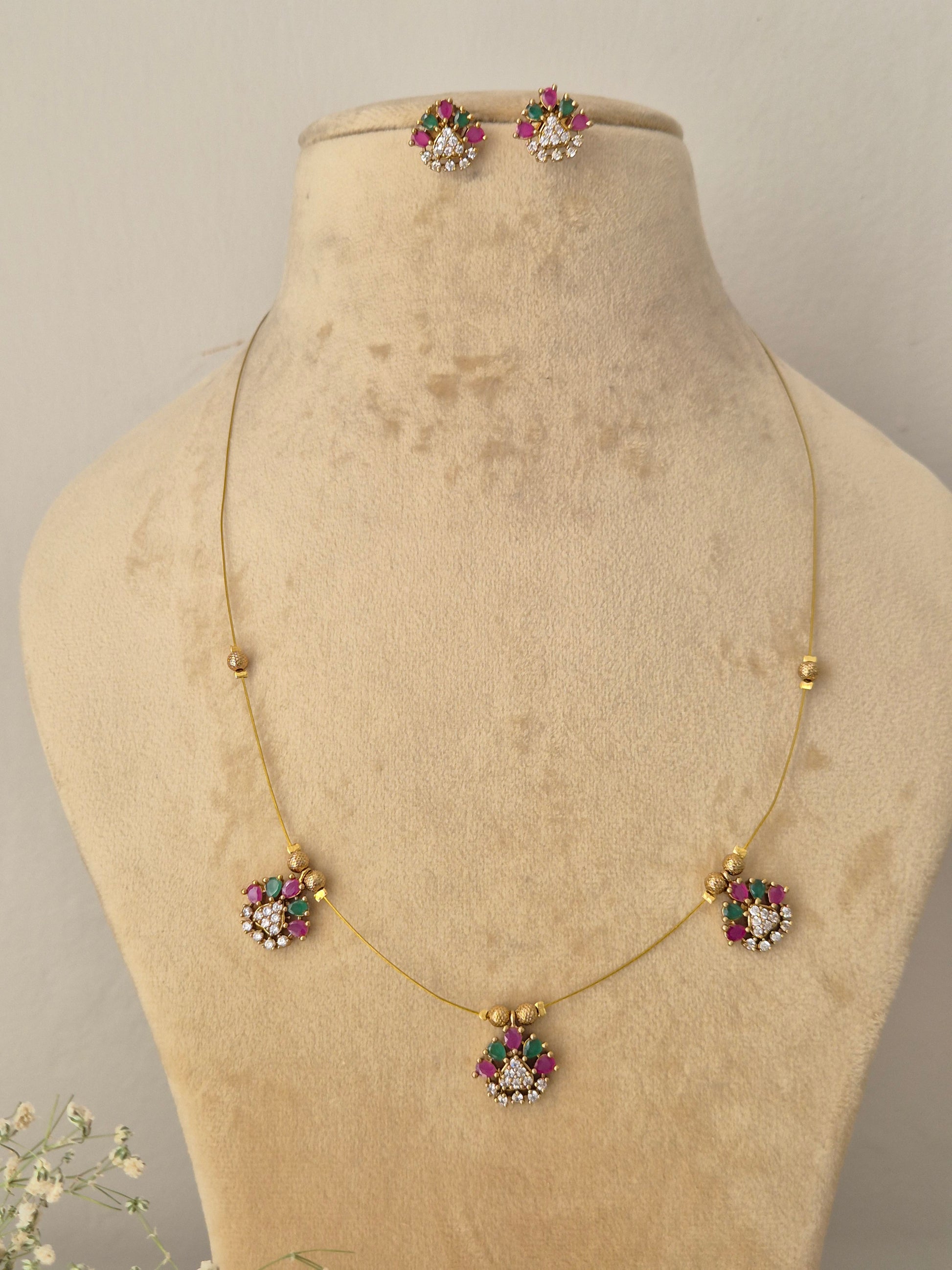 Minimalist gold-toned fine chain necklace featuring three dangling flower charms with pink and green stone petals, coordinating floral stud earrings by naitri.in