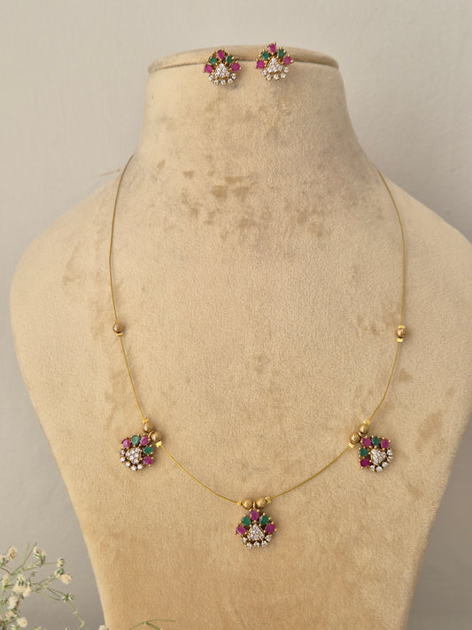 Minimalist gold-toned fine chain necklace featuring three dangling flower charms with pink and green stone petals, coordinating floral stud earrings by naitri.in