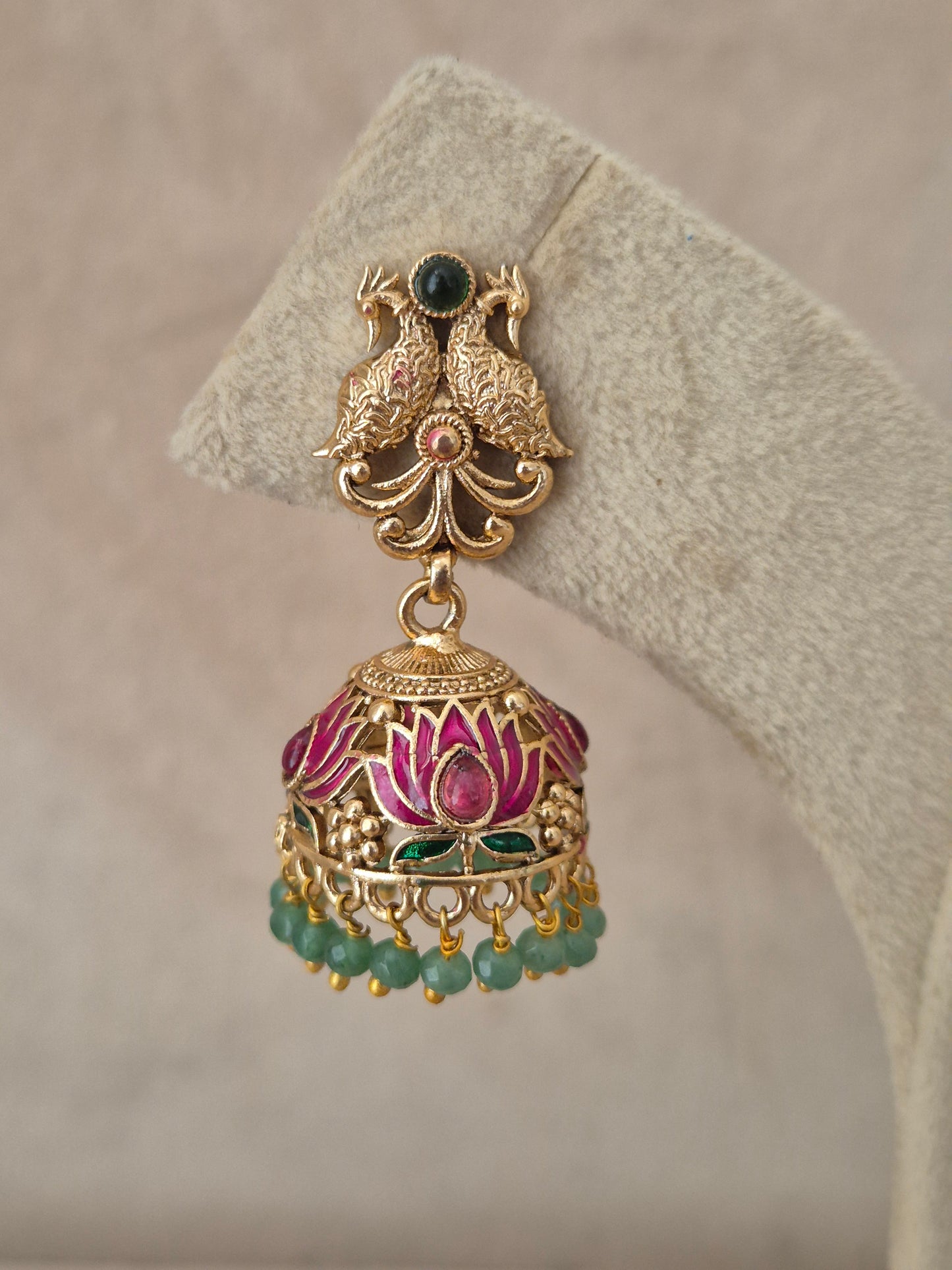 Close-up of Naitri Manorama premium gold ethnic earrings showcasing traditional Indian temple jewelry craftsmanship with vibrant pink and green enamel work and dangling green beads by naitri.in