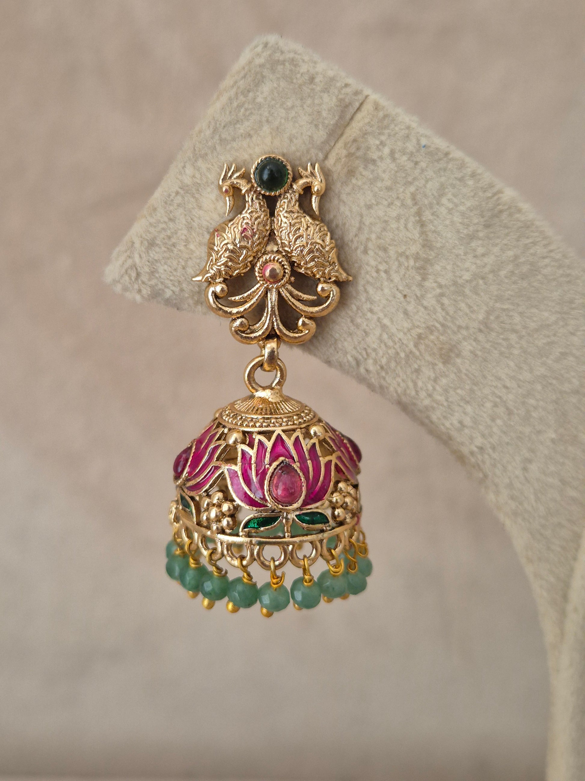 Close-up of Naitri Manorama premium gold ethnic earrings showcasing traditional Indian temple jewelry craftsmanship with vibrant pink and green enamel work and dangling green beads by naitri.in