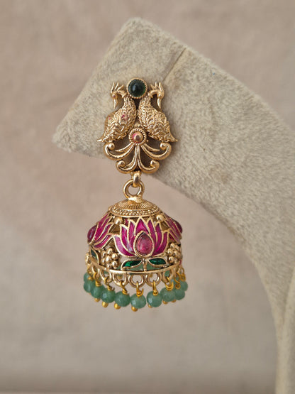 Close-up of Naitri Manorama premium gold ethnic earrings showcasing traditional Indian temple jewelry craftsmanship with vibrant pink and green enamel work and dangling green beads by naitri.in