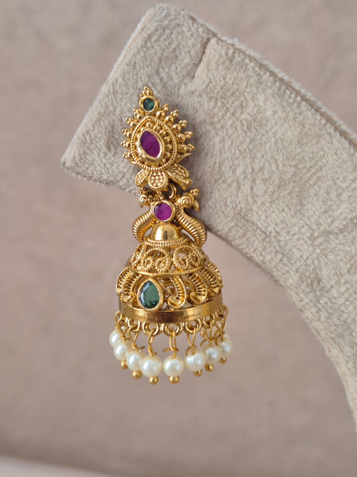 An ornate gold-toned traditional jhumka earring with green and purple stones and white pearl drops, by naitri.in