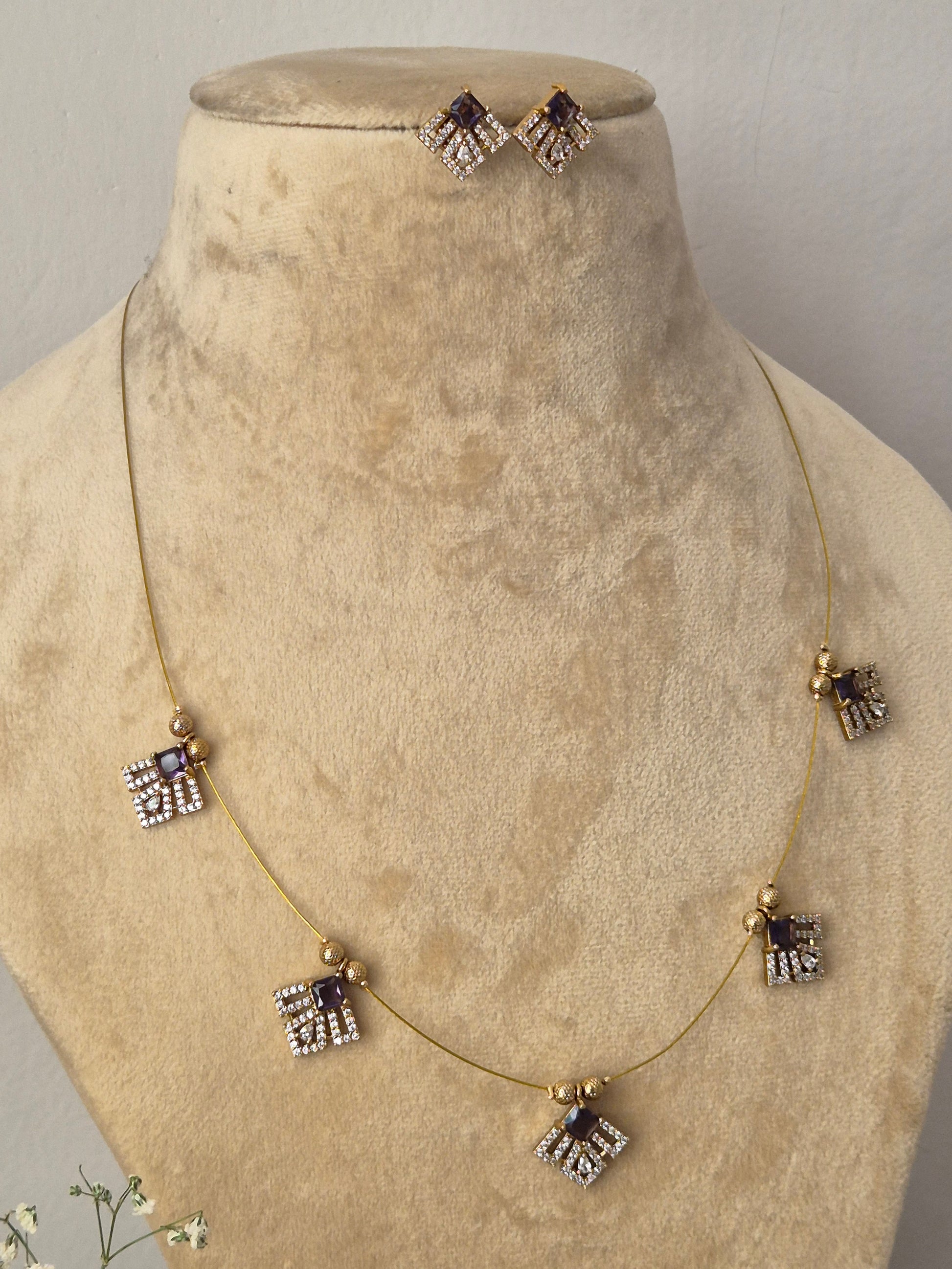 Minimalist gold-toned invisible chain necklace featuring five hanging square-shaped charms accented with purple gemstones and clear crystals, shown with matching square stud earring by naitri.in