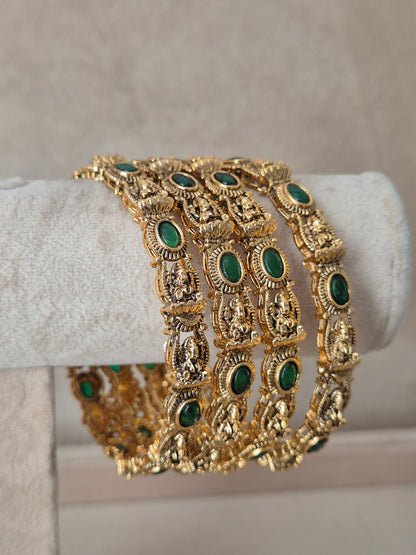 A wide gold-toned bangle bracelet with multiple rows of oval green stone accents, by naitri.in