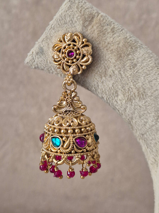 Intricately crafted brass alloy dangle earrings featuring floral top studs, bell-shaped jhumkas with multi-colored stone accents, and dangling red beads by naitri.in