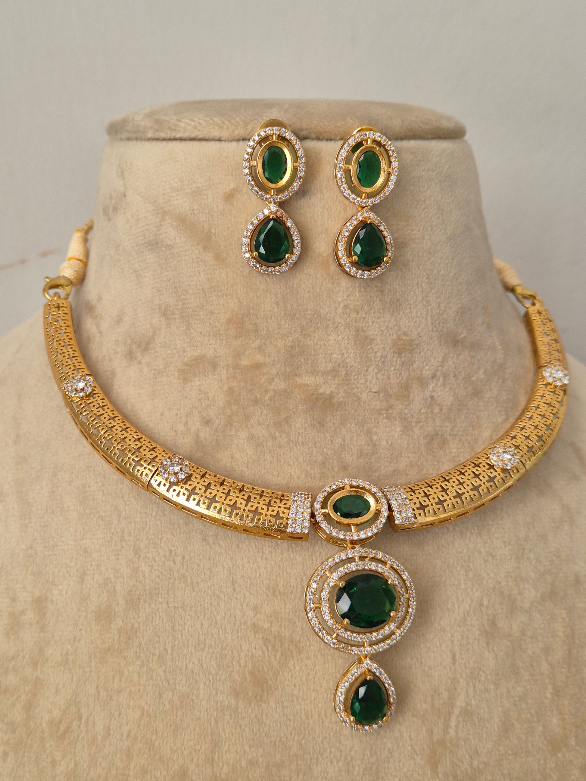 Gold-plated ethnic choker set featuring an openwork filigree band, a prominent oval-cut green stone pendant surrounded by crystals, and matching teardrop earrings by naitri.in