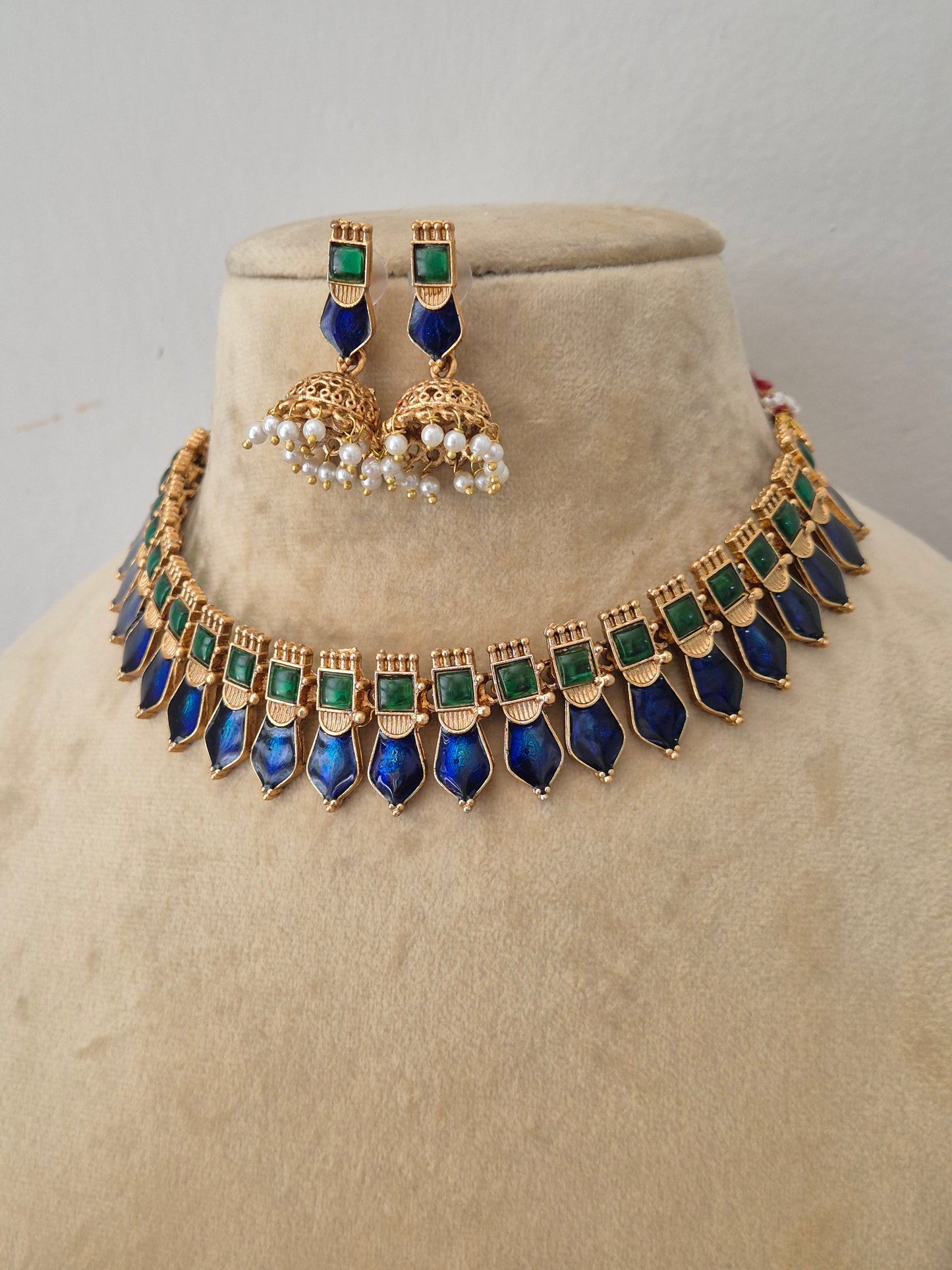 Modern Indian ethnic imitation jewelry set including a golden brass alloy choker necklace embedded with royal blue and emerald green stones, shown with matching dangling earrings featuring tiny white pearl clusters by naitri.in