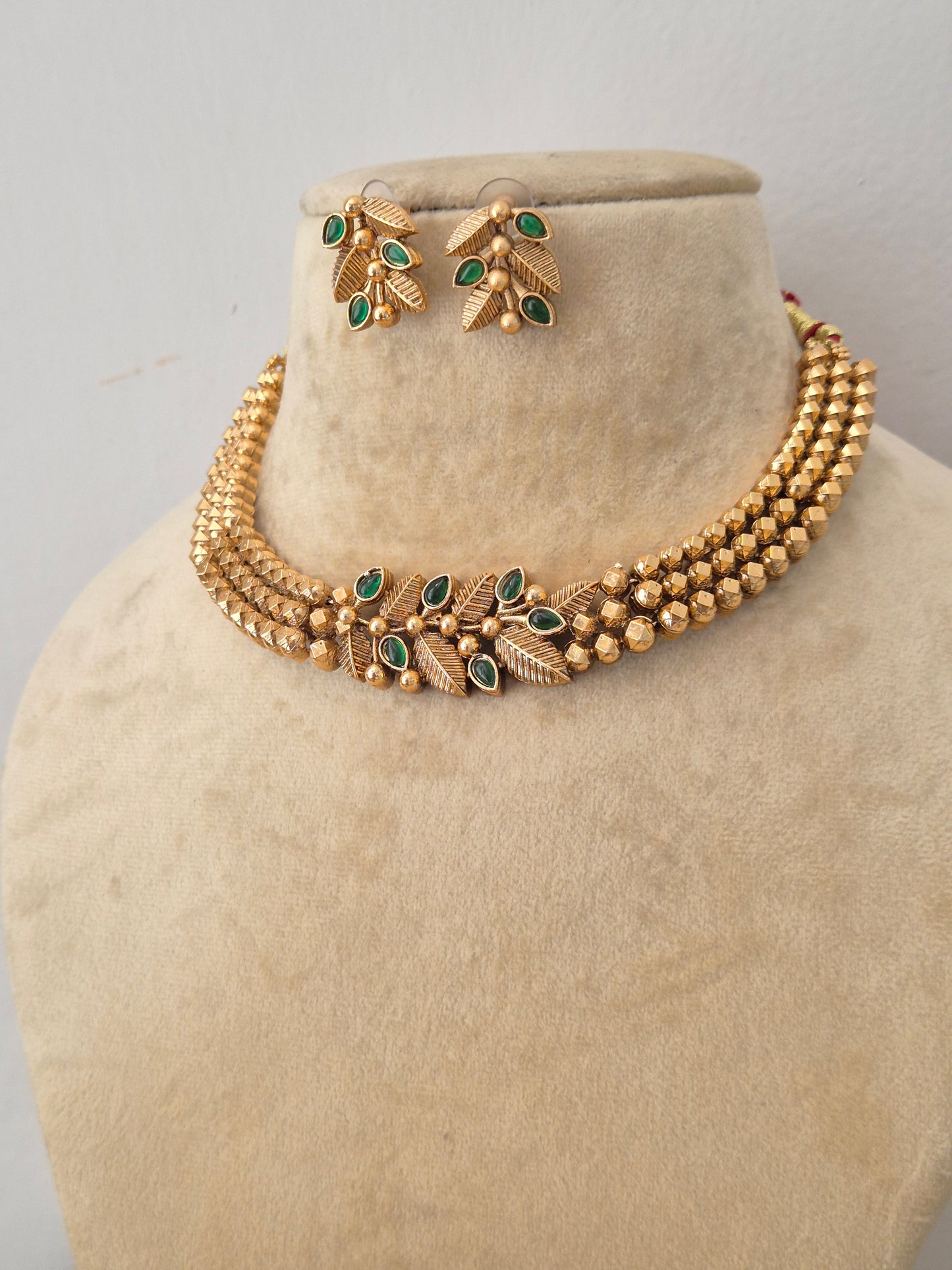 Modern Indian ethnic imitation jewelry set including a multi-layered golden beaded strand choker necklace with emerald green stone details, by naitri.in