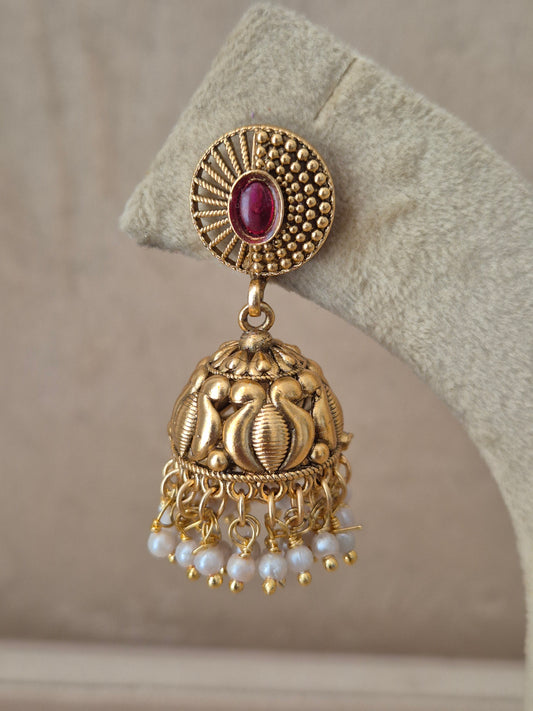Traditional gold-toned temple design Jhumka earrings with a pink gemstone stud and tiny white pearl drops by naitri.in