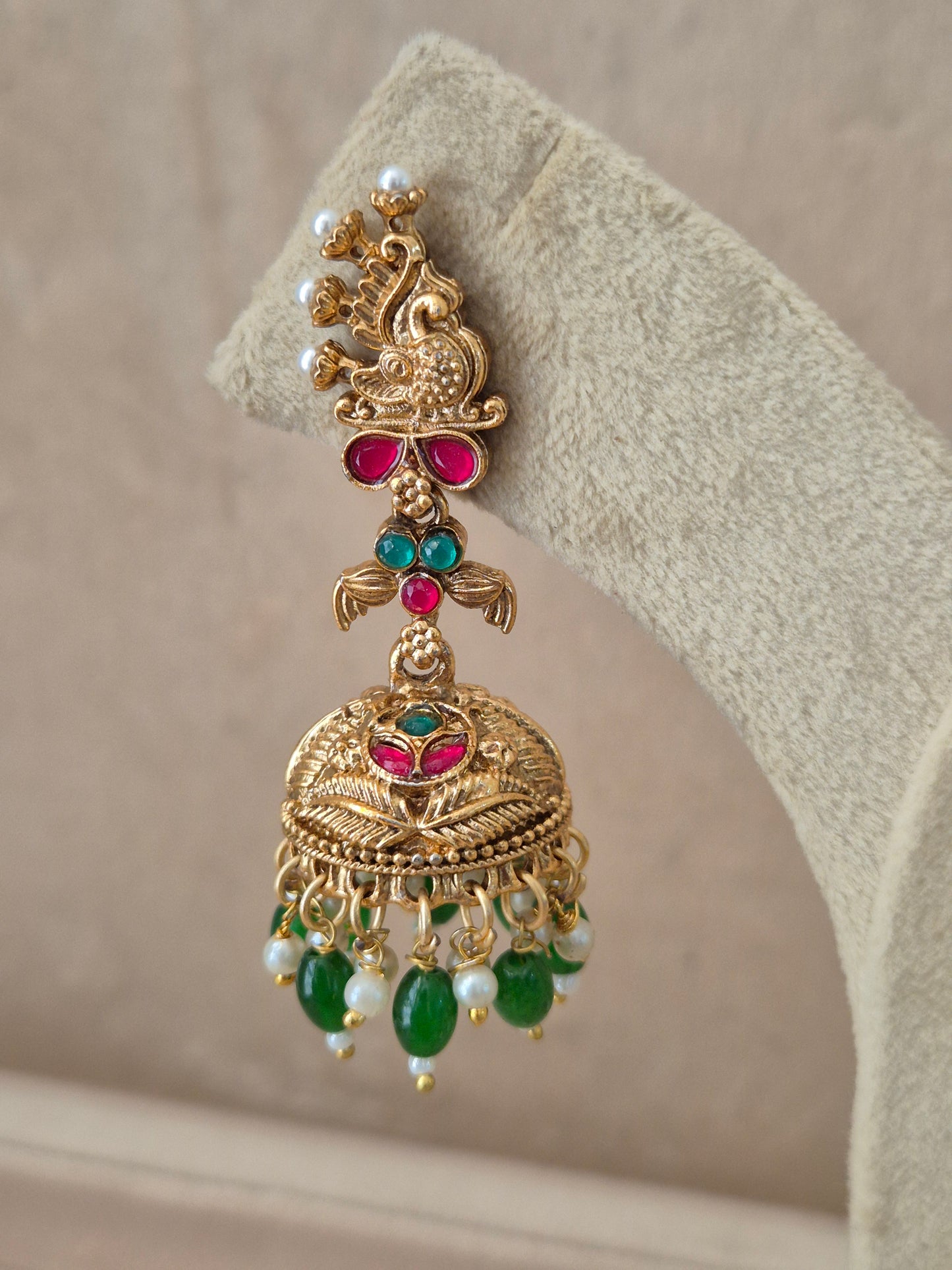 Close-up of Naitri Oindrila premium gold ethnic earrings showcasing traditional Indian temple jewelry craftsmanship with vibrant ruby red and emerald green stones and dangling bead details by naitri.in