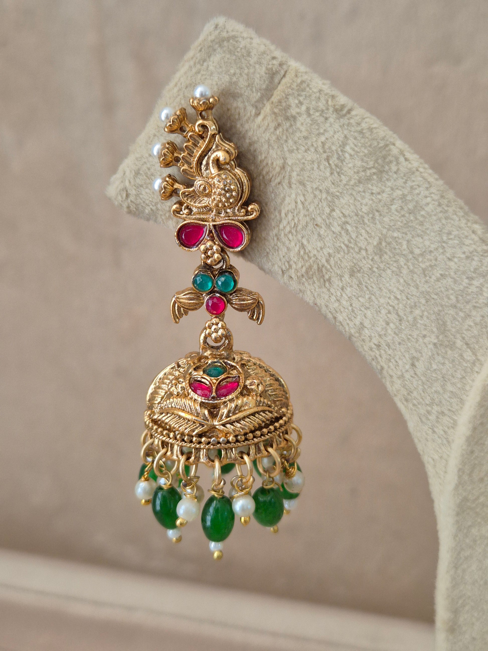 Close-up of Naitri Oindrila premium gold ethnic earrings showcasing traditional Indian temple jewelry craftsmanship with vibrant ruby red and emerald green stones and dangling bead details by naitri.in