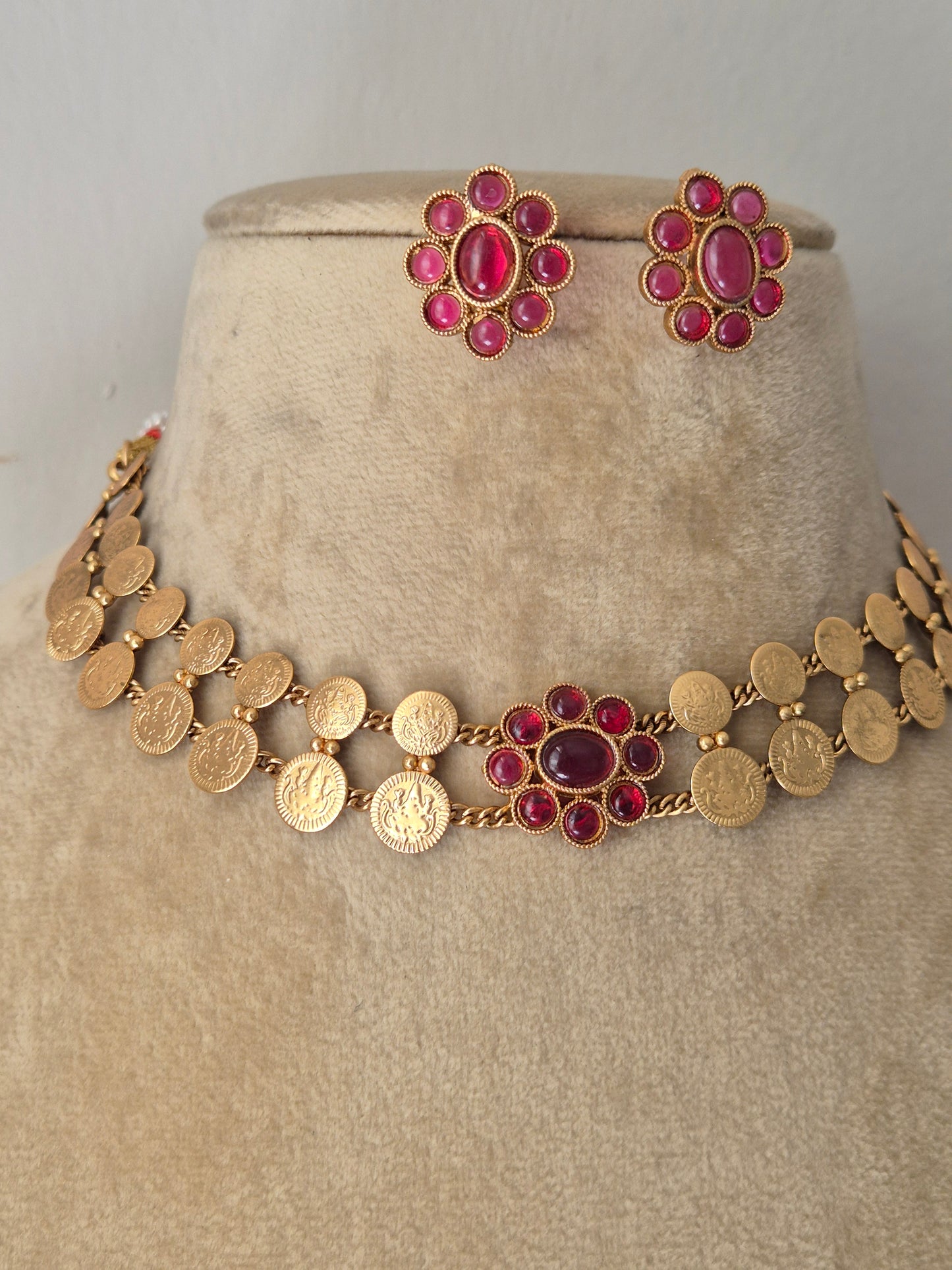 Gold-plated ethnic choker set composed of two rows of textured circular discs and a central ruby-pink gemstone flower, shown with matching flower stud earrings by naitri.in
