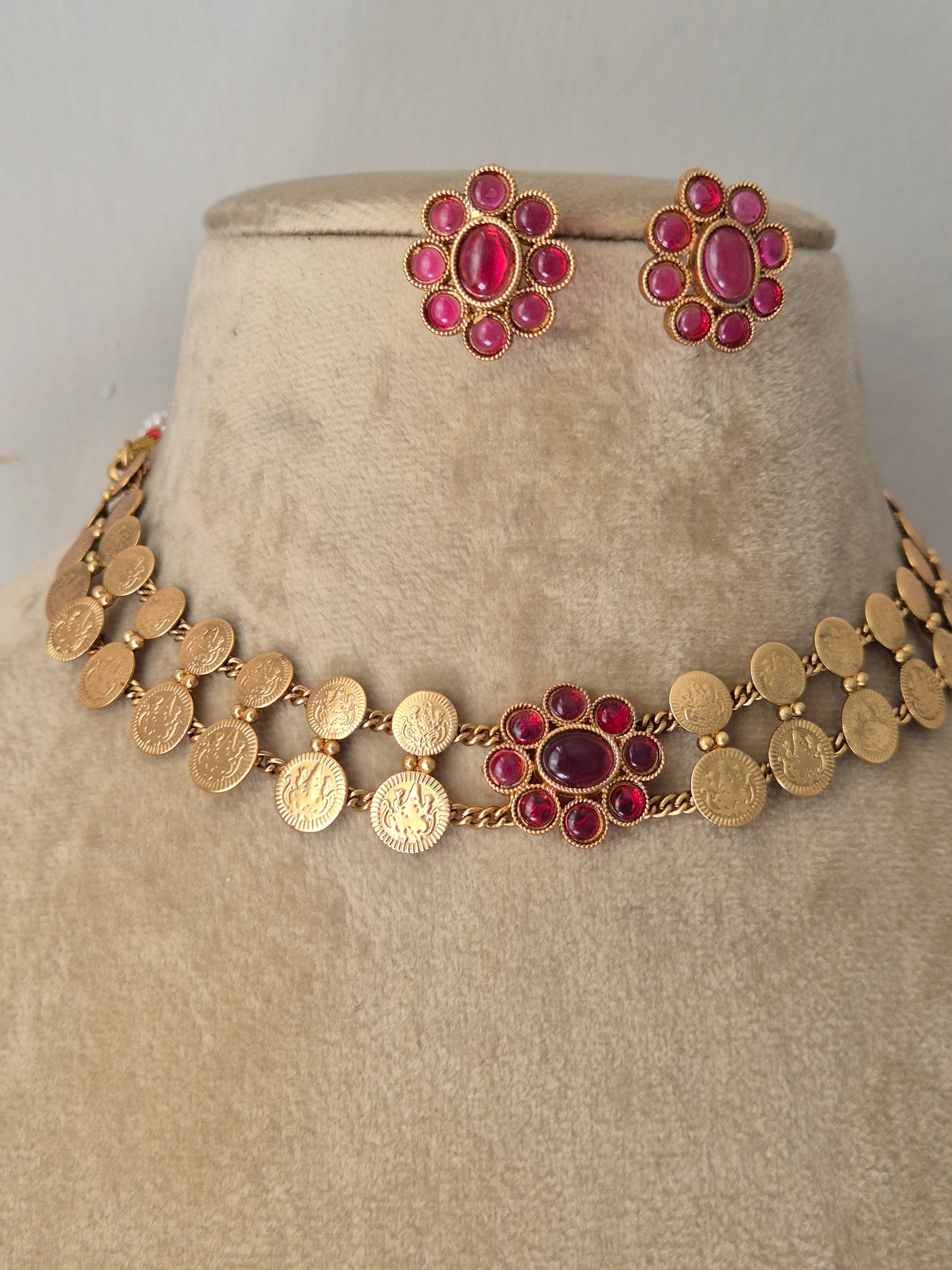 Gold-plated ethnic choker set composed of two rows of textured circular discs and a central ruby-pink gemstone flower, shown with matching flower stud earrings by naitri.in