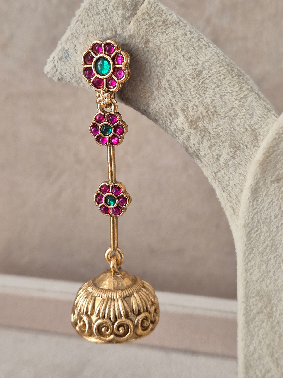 Gold-plated long dangling jhumka earrings featuring a vertical drop of ruby-red and emerald-green stone clusters leading to an intricate bell-shaped dome by naitri.in