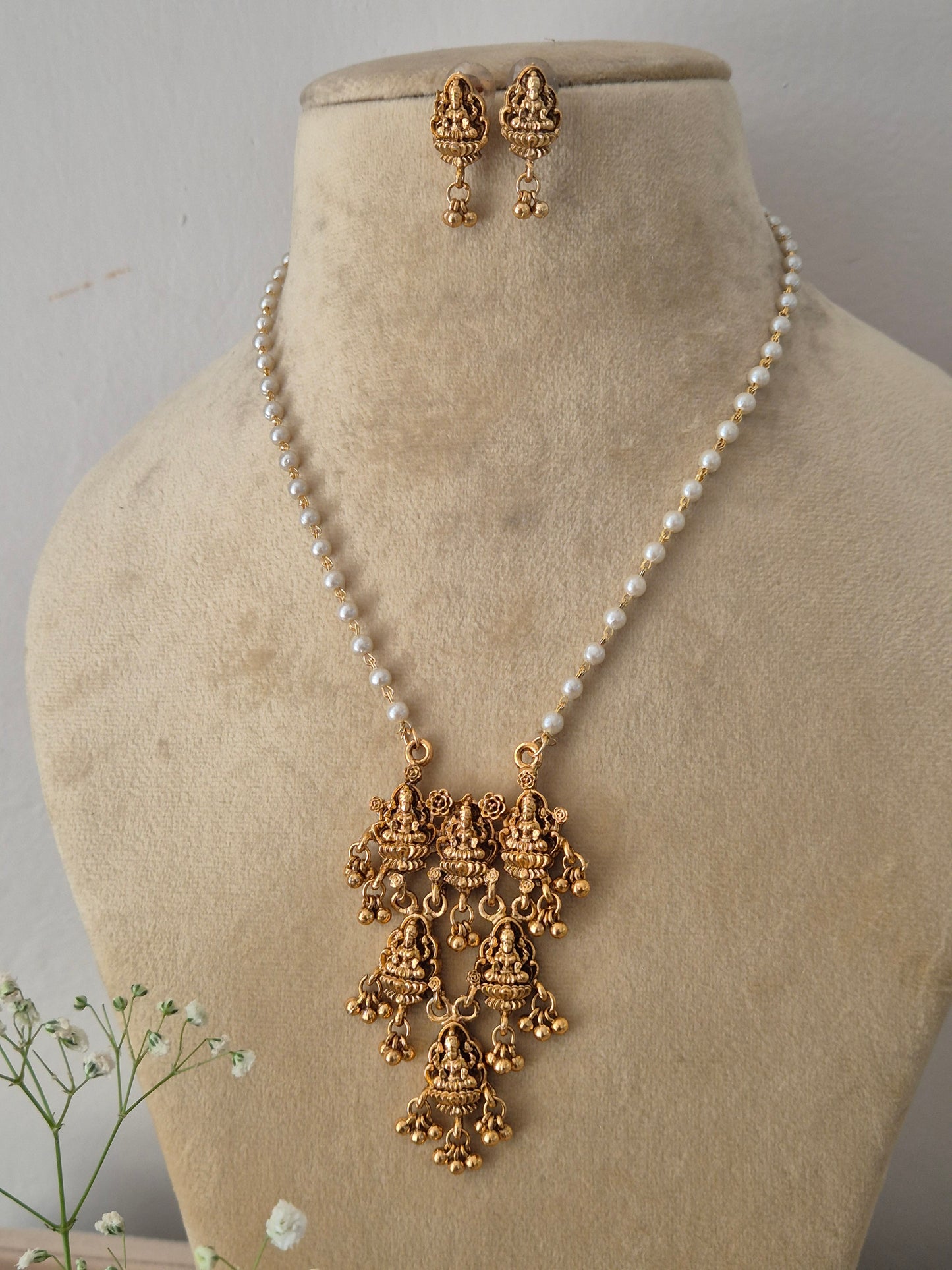 Elegant gold-toned traditional Indian pendant necklace set with pearl chain details, showcased on a minimalist by naitri.in 