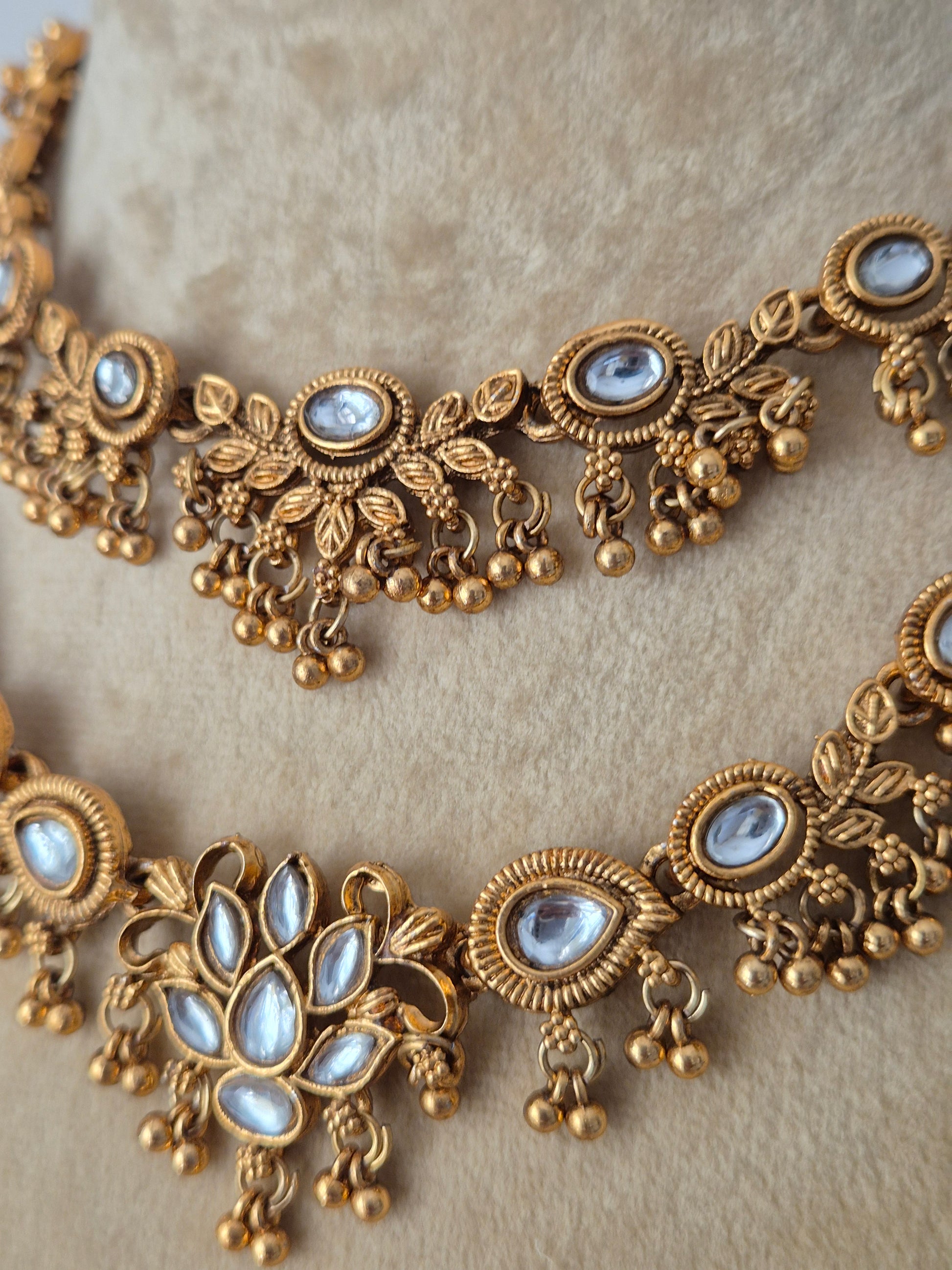 Traditional Indian antique gold-finish brass necklace set showcasing two tiered layers of intricate floral carvings, white stone accents, and coordinating festive earrings from the Naitri collection by naitri.in