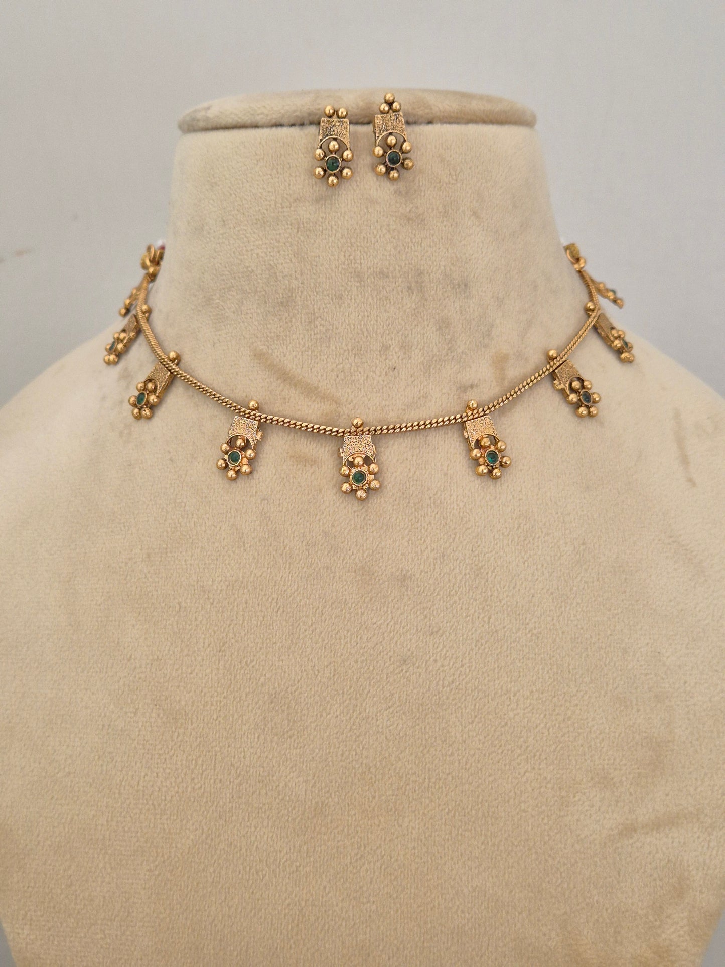 Traditional Indian gold-toned choker necklace with delicate hanging floral charms accented with green gemstones by naitri.in